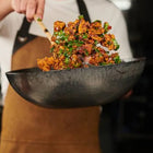Chef tossing crispy seasoned cauliflower with herbs in a large bowl.