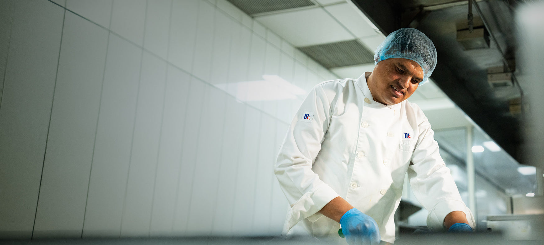 Chef in a white McCormick coat and hairnet preparing food in a commercial kitchen.