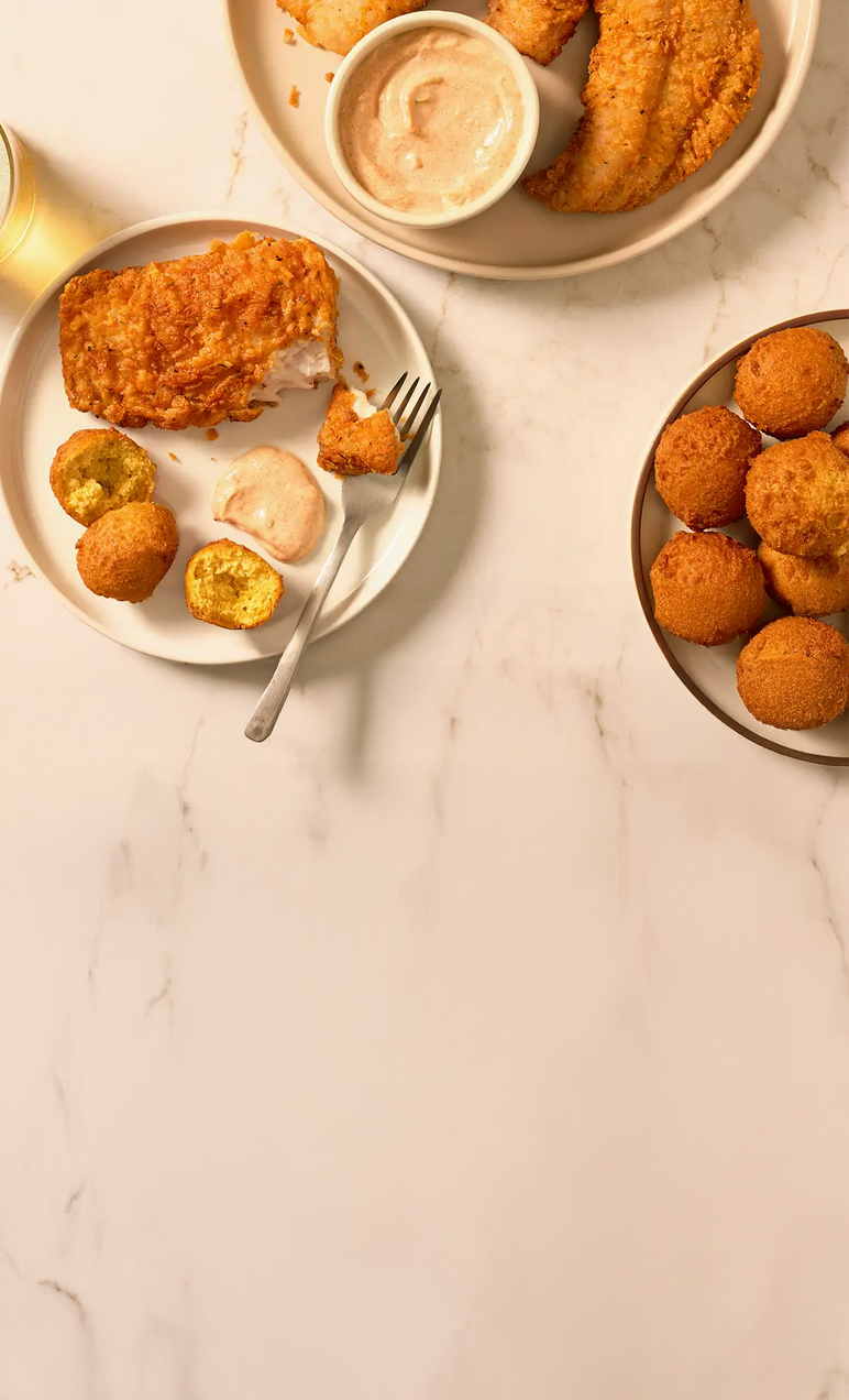 Fried chicken, hush puppies, and sides on a marble surface