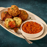 Assorted falafel balls on a plate with a bowl of red sauce on a blue background