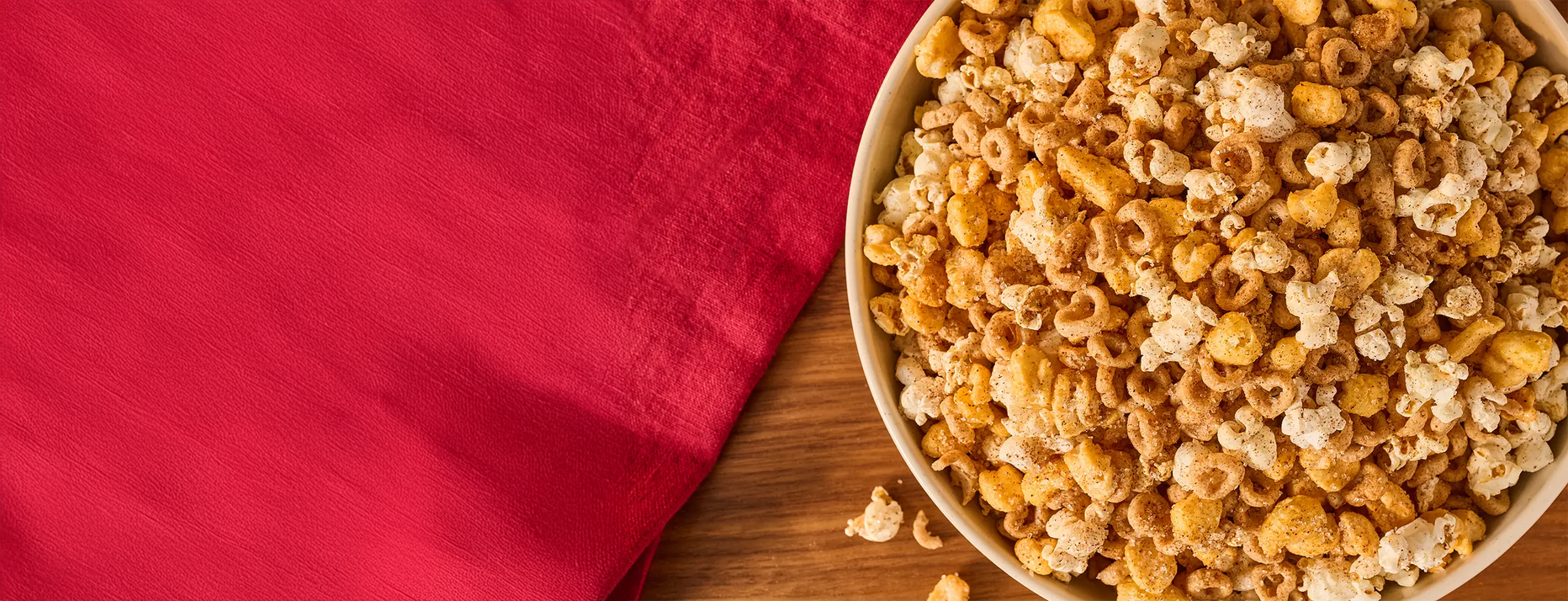 Bowl of popcorn on a wooden surface with a red cloth background