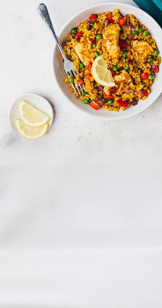  bowl of colorful paella with lemon wedges on a white surface
