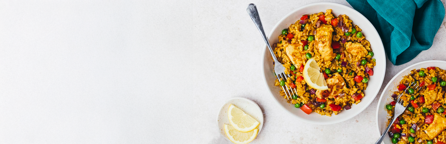 Two bowls of colorful paella with lemon wedges on a white surface