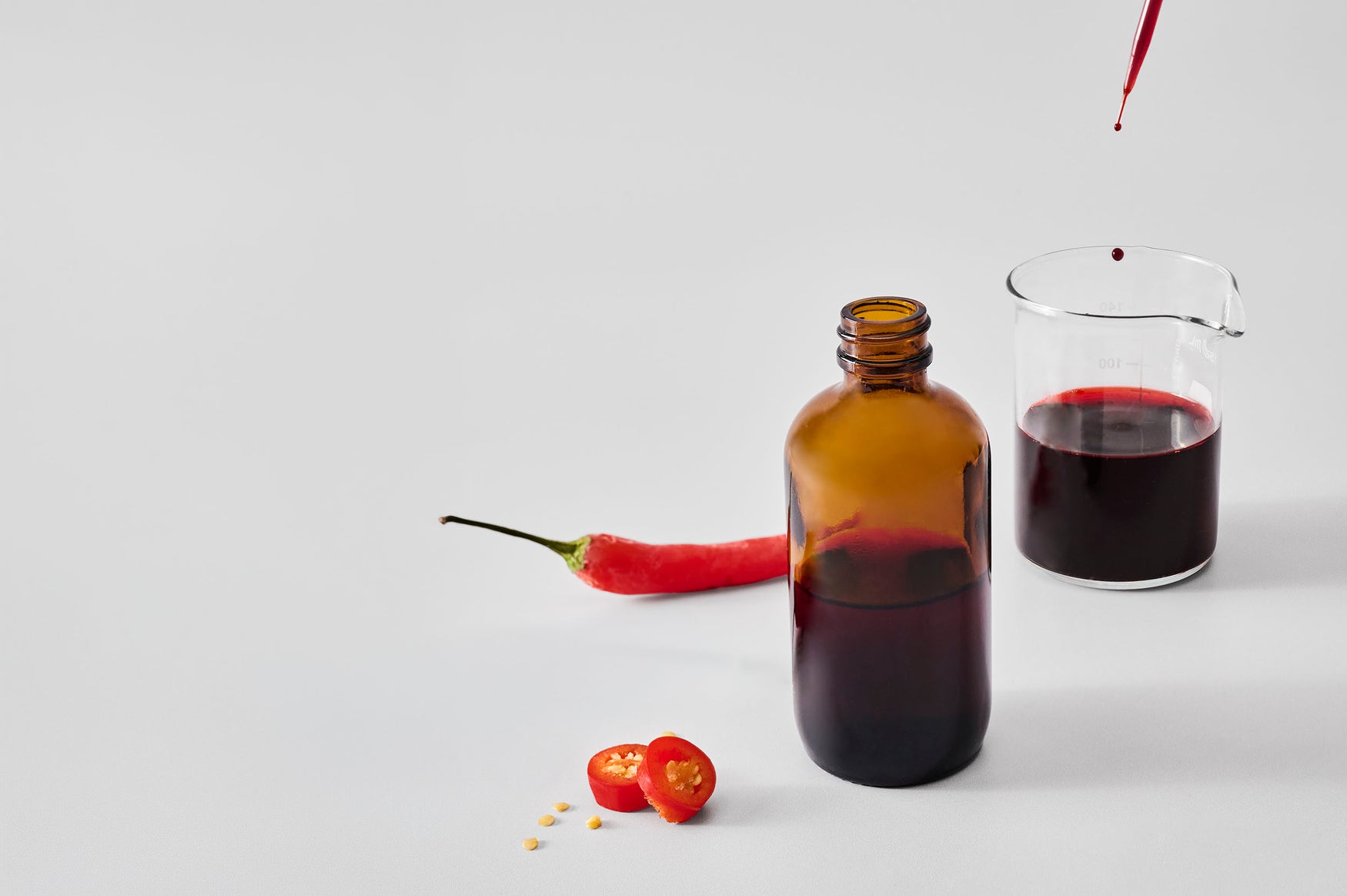 Chili extract in glass bottle with red chili peppers on white background