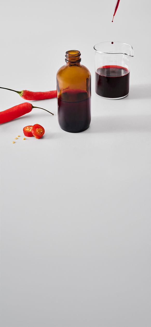 Pipette dropping red chili extract into a beaker beside a bottle and fresh red chilies.