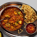 Chicken curry in a serving pan with naan bread and chutney.