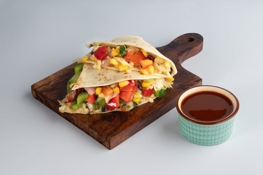 Colorful wrap on a wooden board with a side of dipping sauce on a light gray background