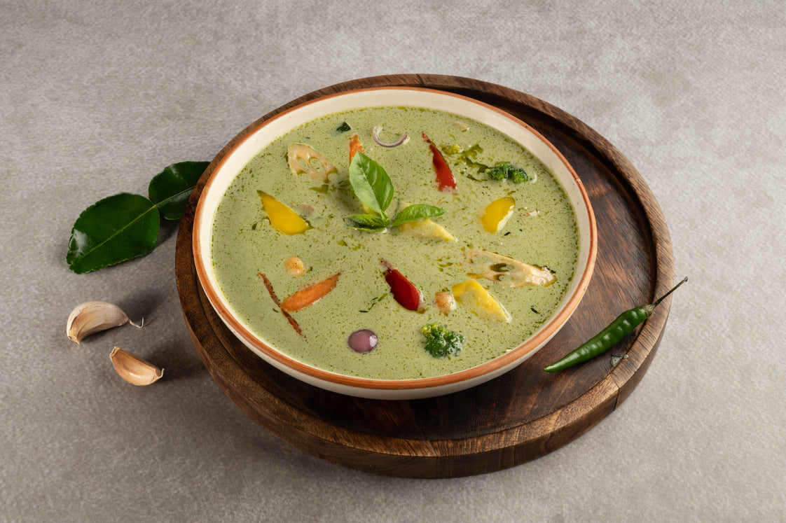 Green soup in a bowl on a wooden tray with garnishes on a gray background