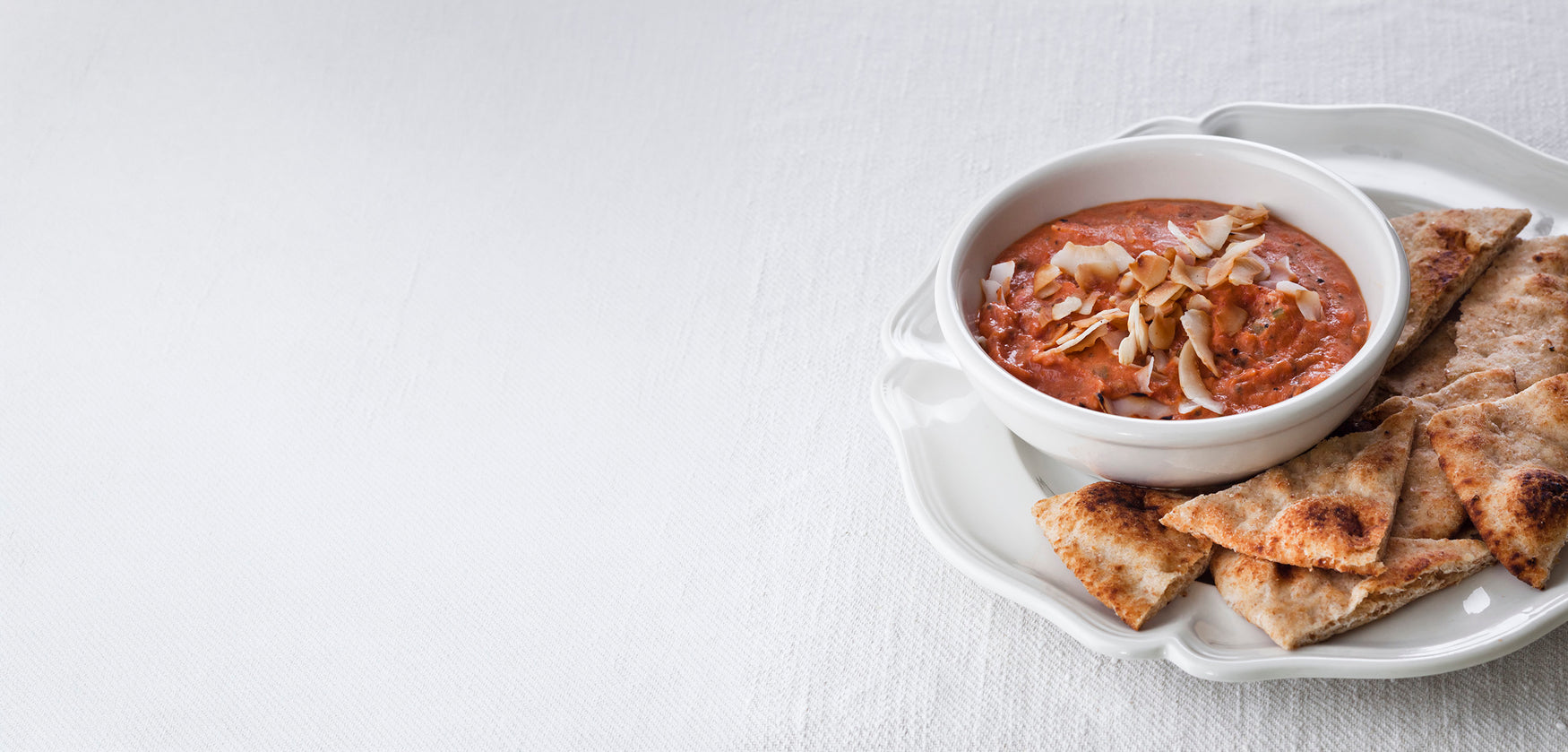 Creamy red dip topped with sliced almonds and served with toasted flatbread pieces.