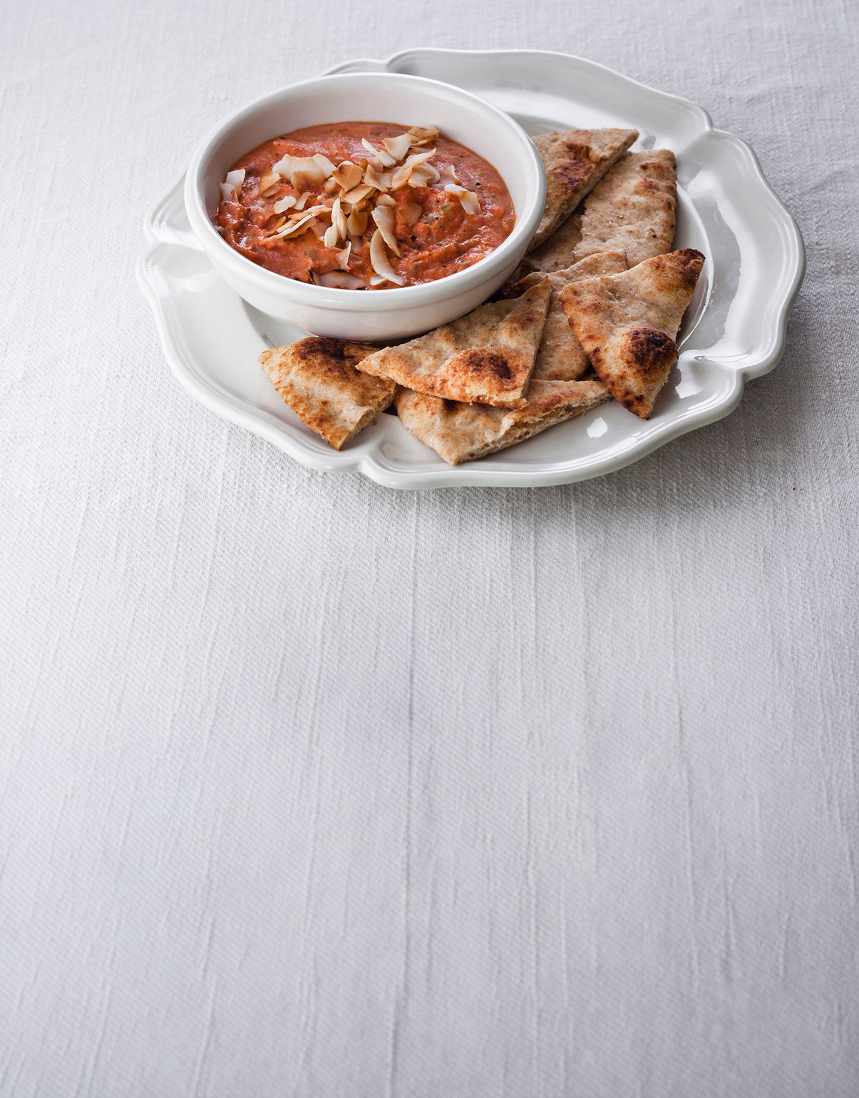 Creamy red dip topped with sliced almonds and served with toasted flatbread pieces.